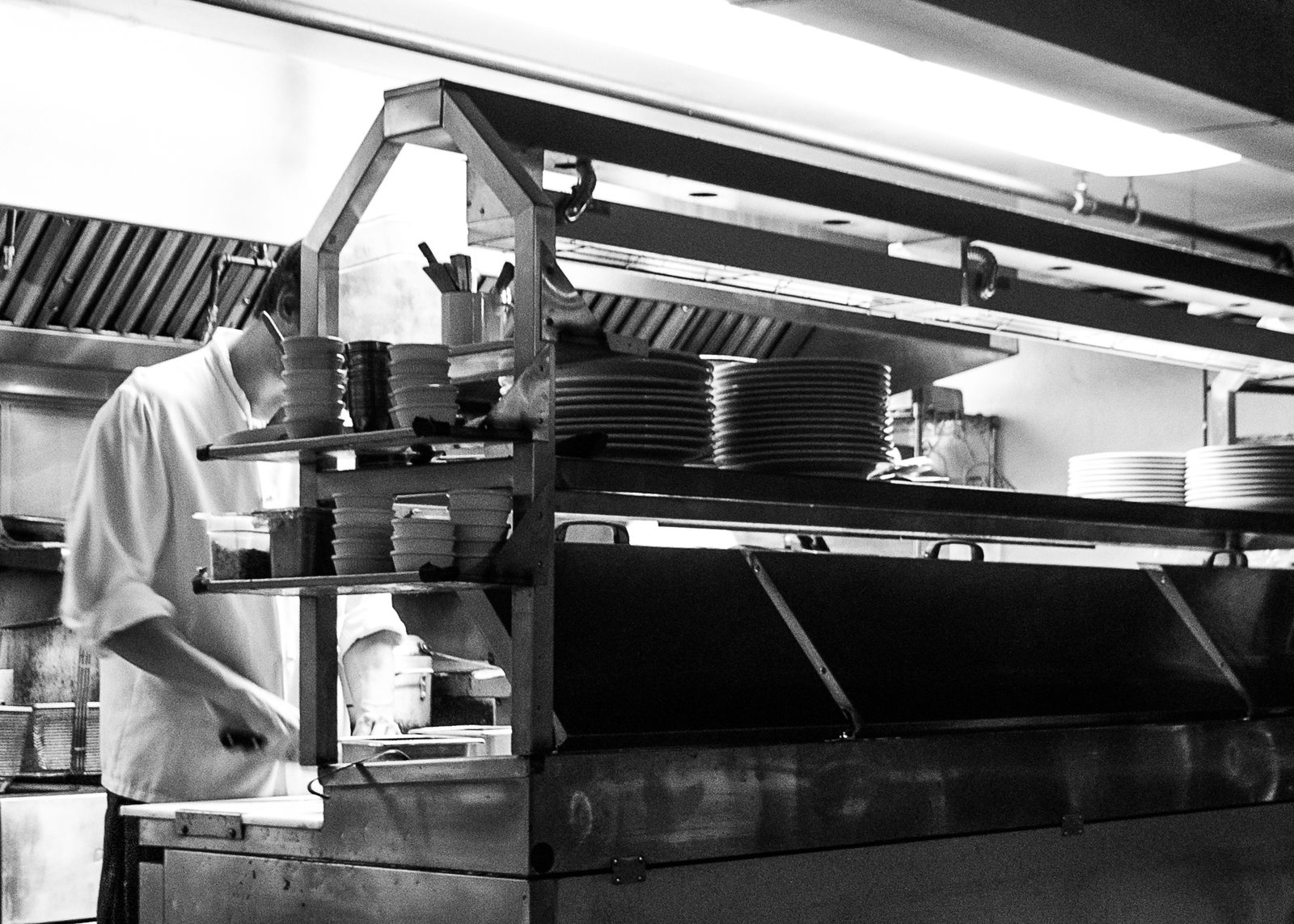 A line cook working at the pass of a restaurant kitchen late at night