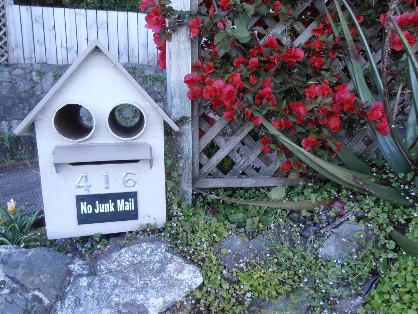 A homemade letter box with a No Junk Mail sign in a garden