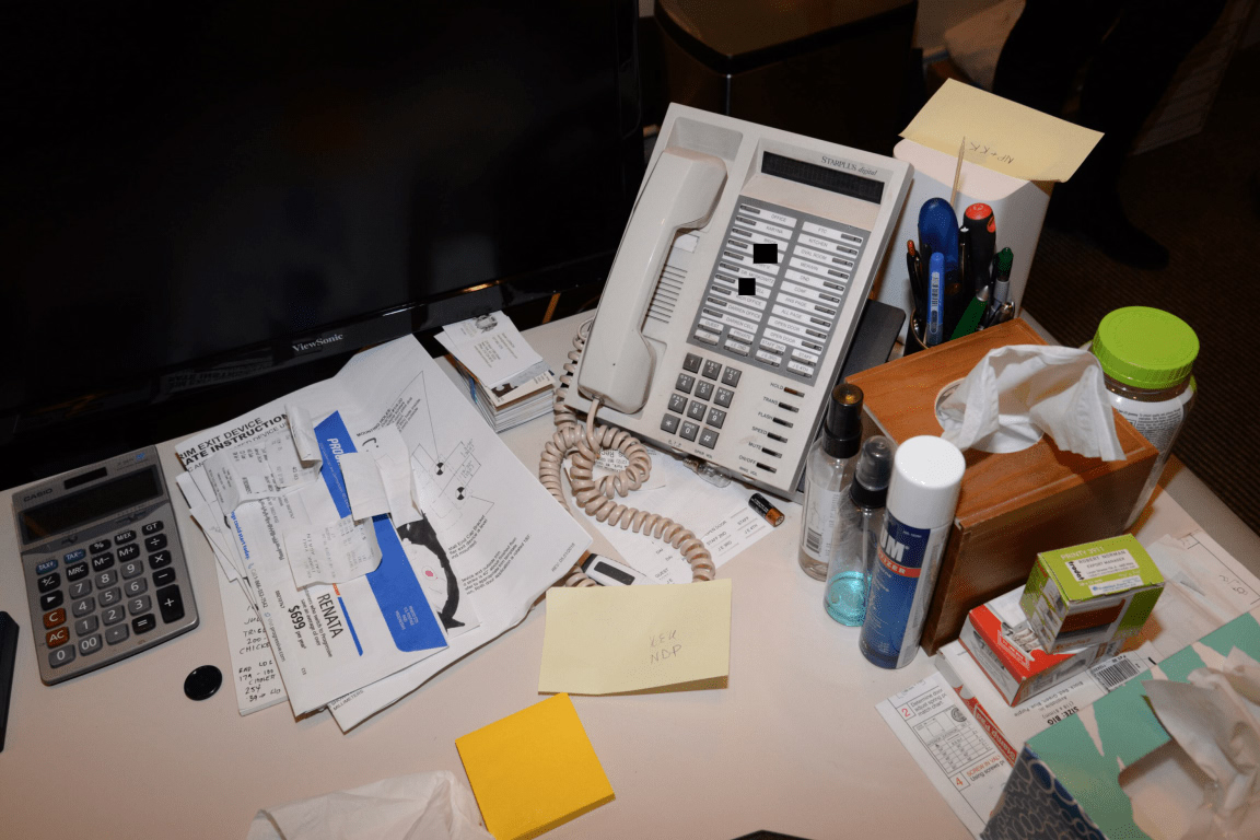 A cluttered desk with phone, calculator, papers, and pens — the visual reality of an office where the audit has been deferred.